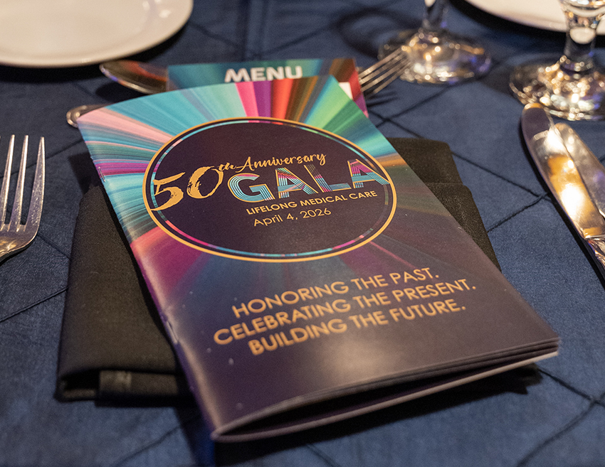 LifeLong Medical Care 50th Anniversary Gala printed program booklet on a dinner table setting, reading "Honoring the Past. Celebrating the Present. Building the Future." — April 4, 2026