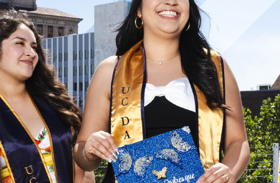 UC Davis graduate holding a decorated cap reading "Para mis Padres que llegaron sin nada pero me lo dieron todo" (For my parents who arrived with nothing but gave me everything), celebrating with a fellow student at graduation