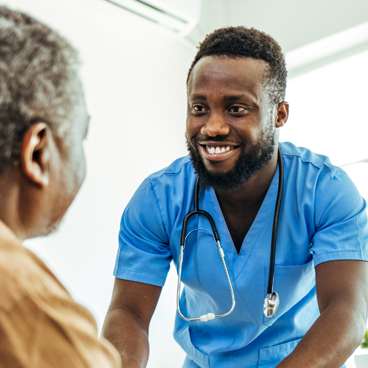 Square portfolio image of a smiling healthcare worker in blue scrubs with a stethoscope engaging warmly with a patient, representing the human-centered focus of the RUHS workforce development report